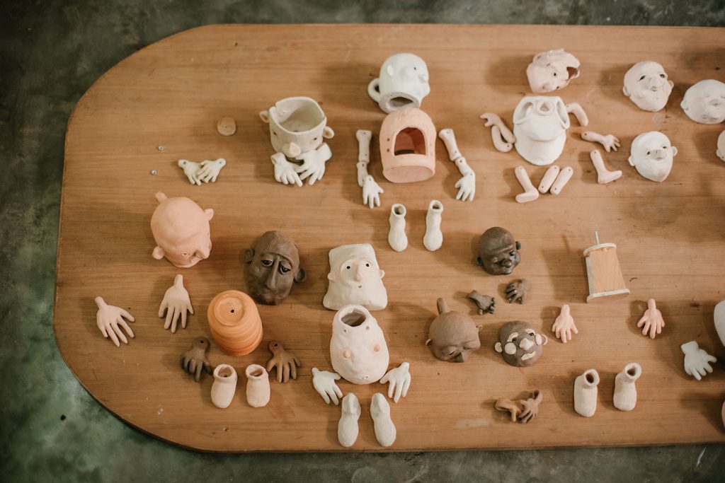 写真：机の上に並んだ人形の顔、手、足などいろんなパーツ