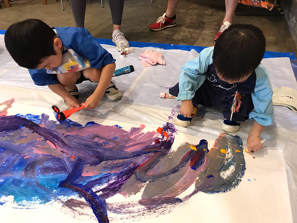 写真：大きな紙の上に乗って色を塗る2人の男の子