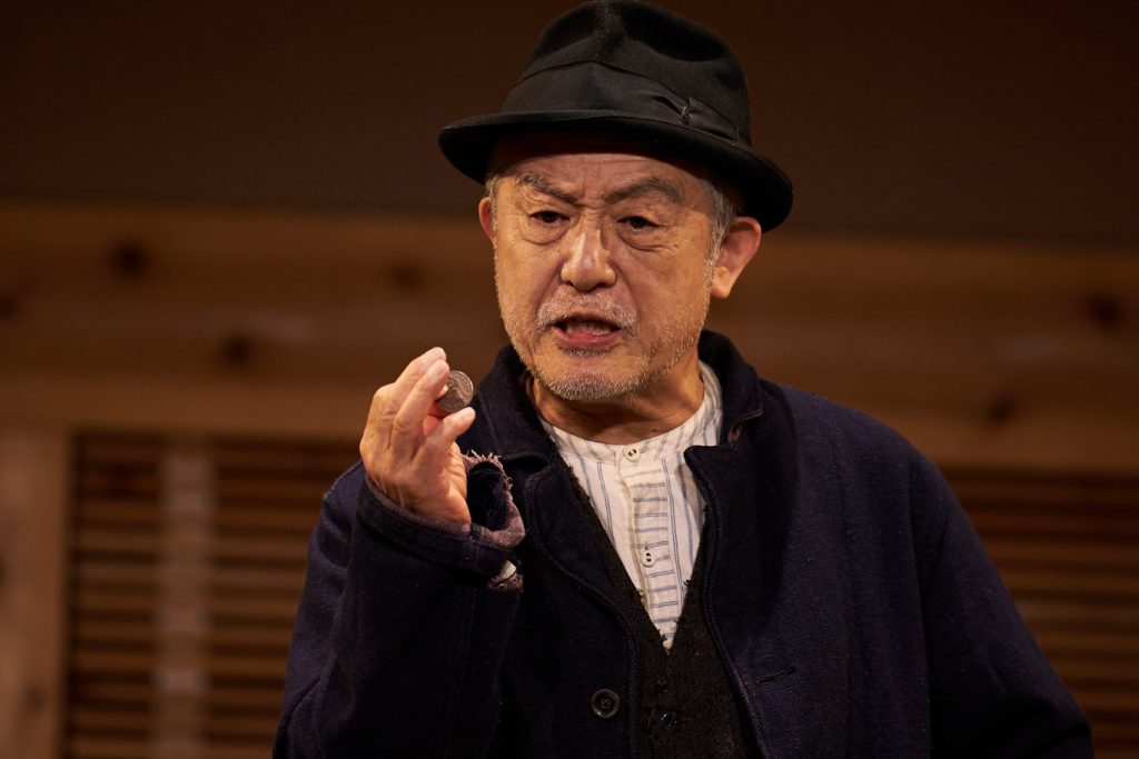 写真：1人芝居中の串田さん。コインを手に持っている。