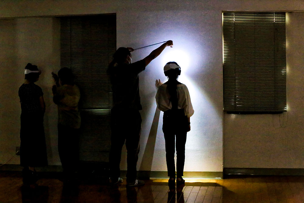 写真：ライトで壁を照らす人と、ゴーグルをかけて壁を見る人。
