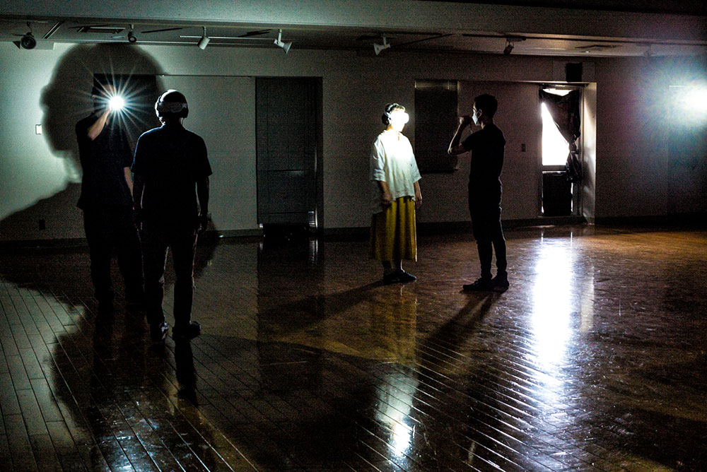 写真：ゴーグルをかけた参加者と、ライトを持ったガイドが2人1組で作品を体験している。