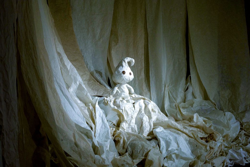 写真：カーテンのように掛かった和紙の中に、紙の人形が立っている。