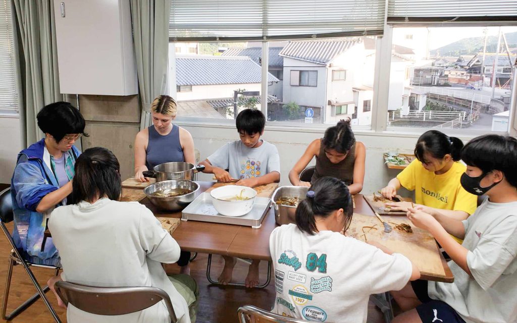 写真：地域の人とテーブルを囲んで、和紙づくりの作業をしているところ